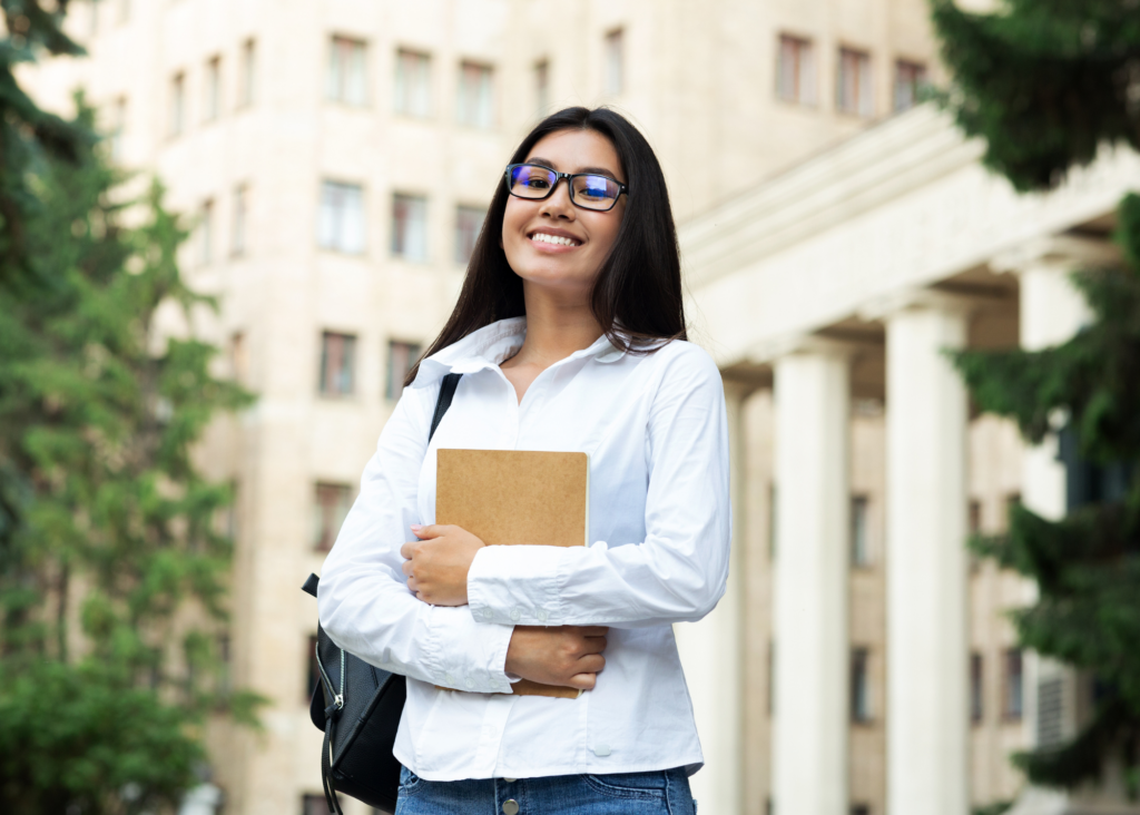 Student with backpack and notebook standing in front of school building.