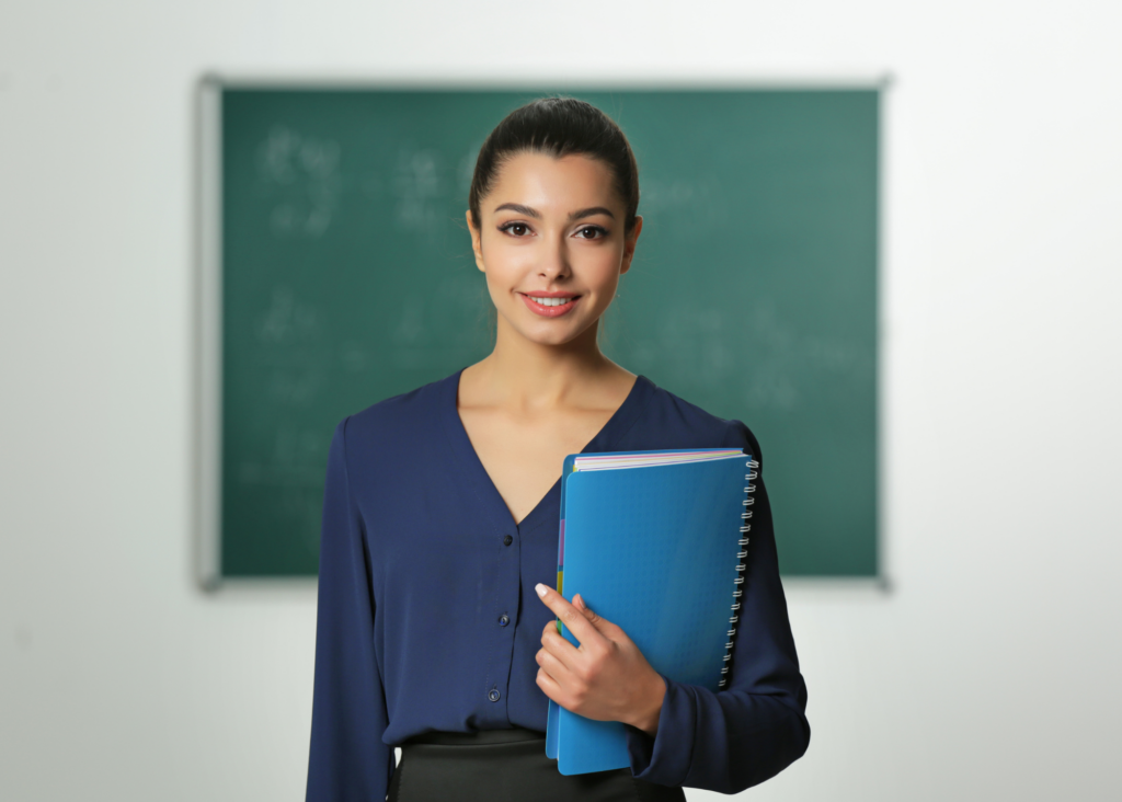 Woman standing in front of a chalk board holding a blue notebook.