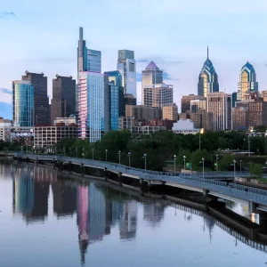 Philadelphia skyline with tall buildings reflected in the Schuylkill River at dusk.